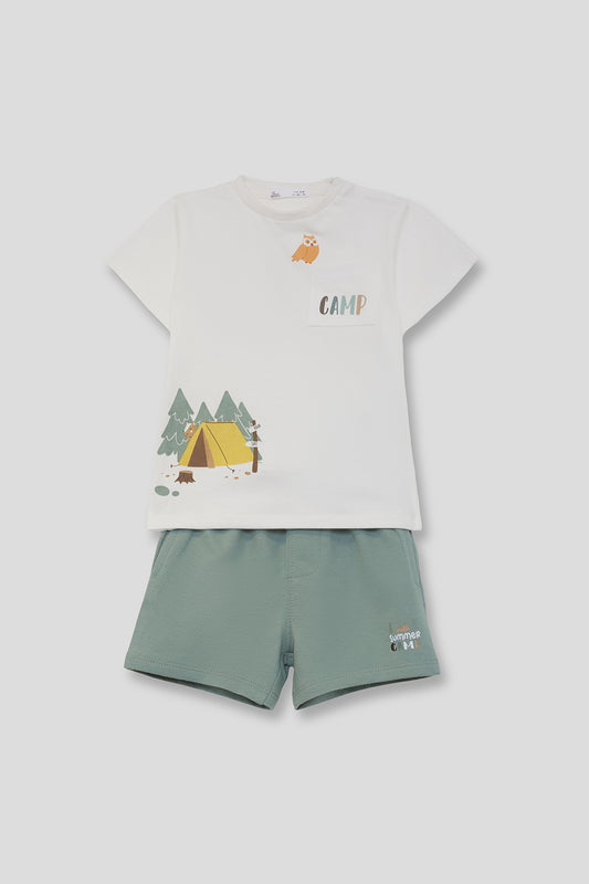 Conjunto infantil de verano con camiseta blanca estampada con tienda de campaña, árboles y palabra “Camp”, y short verde con detalle lateral, sobre fondo neutro.