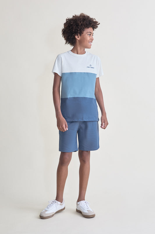 Niño con conjunto de verano compuesto por camiseta blanca y azul con efecto degradado y short azul a juego, sobre fondo claro.