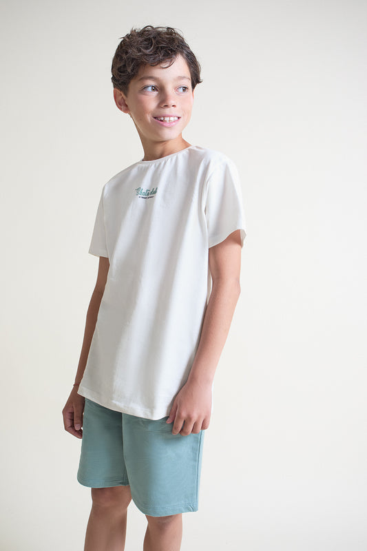 Conjunto infantil de verano con camiseta blanca estampada con cuadros “Street Skate Club” en tonos verde y azul, y short verde menta con bolsillo trasero, sobre fondo neutro.