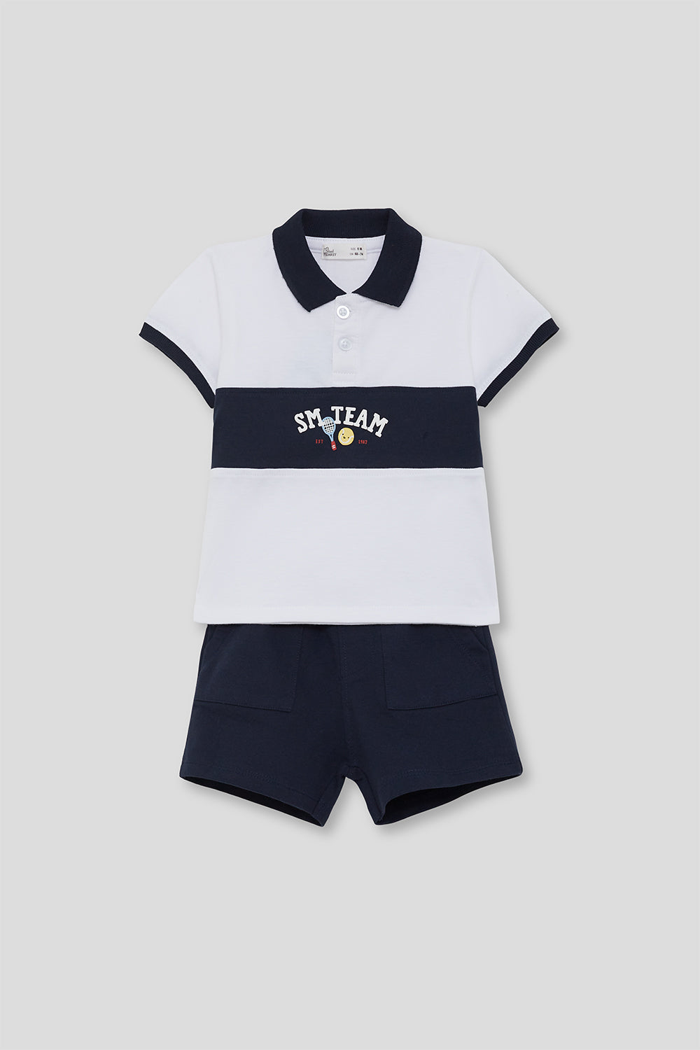 Conjunto infantil de verano compuesto por polo blanco con franja azul marino y bordado “SM Team”, y short azul marino a juego, sobre fondo neutro.