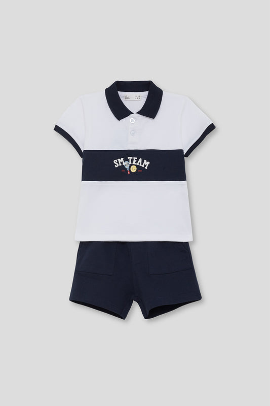 Conjunto infantil de verano compuesto por polo blanco con franja azul marino y bordado “SM Team”, y short azul marino a juego, sobre fondo neutro.