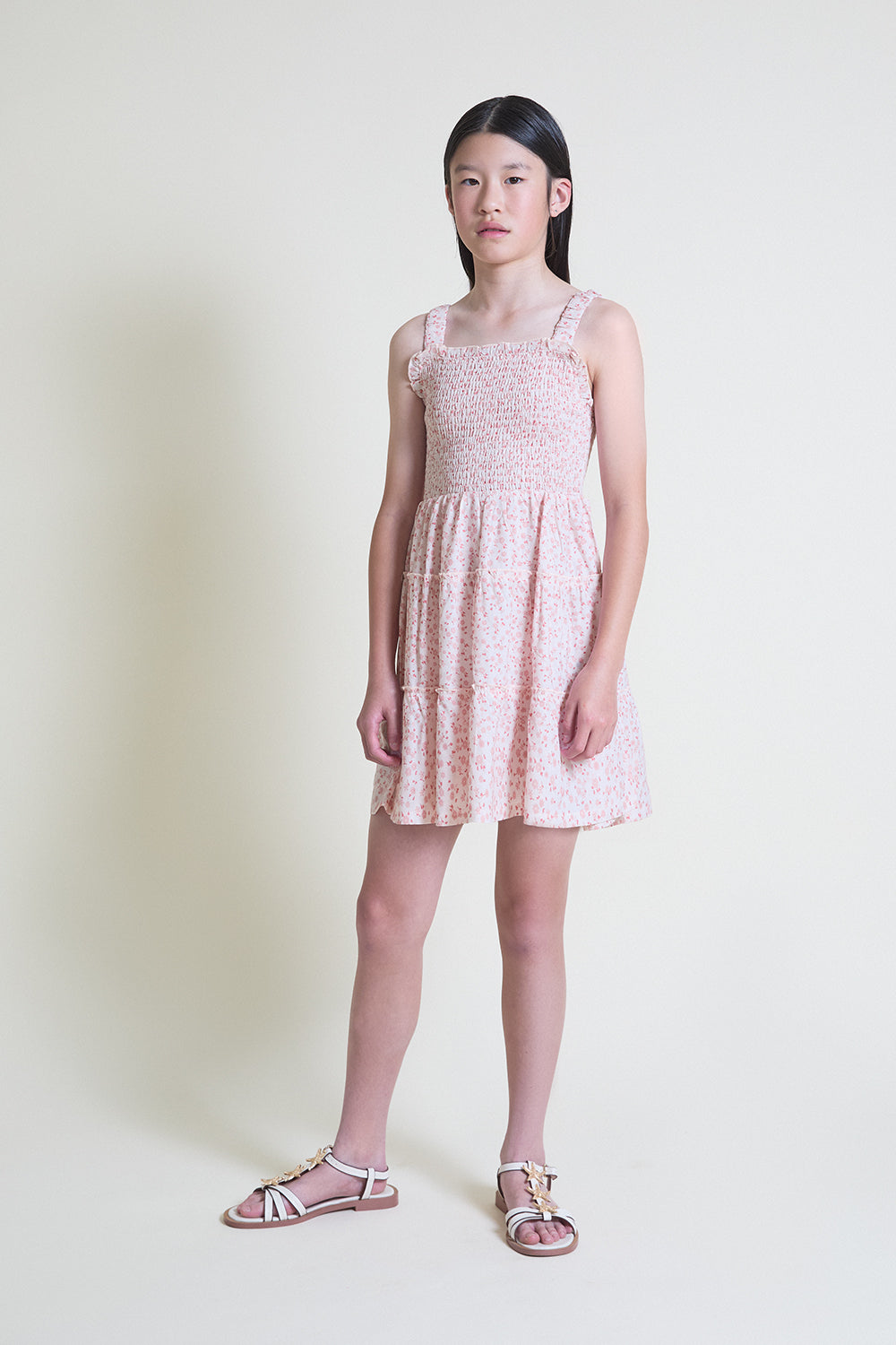 Niña con vestido de verano sin mangas con tirantes finos, cuerpo fruncido y estampado floral en tonos rosa y crudo, ideal para días cálidos.